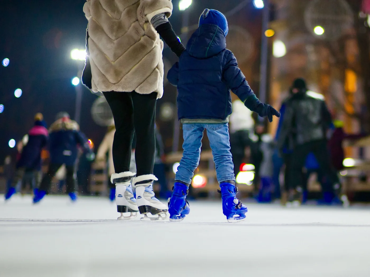 Kind und Mutter Hand in Hand beim Eislaufen unter Abendlichtern